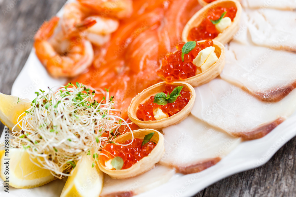 Seafood platter with salmon slice, pangasius fish, red caviar, shrimp, decorated with olives and lemon on wooden background close up. Mediterranean appetizers. Top view Seafood platter with salmon slice, pangasius fish, red caviar, shrimp, decorated with olives and lemon on wooden background close up. Mediterranean appetizers. Top view