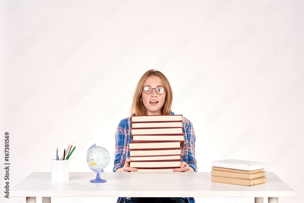 Beautiful teenage schoolgirl sitting at desk with stack of books on it Beautiful teenage schoolgirl sitting at desk with stack of books on it