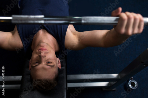 young man flexing muscles with bar in gym