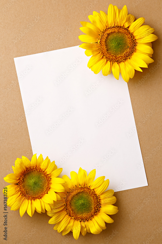 Fototapeta premium Sunflowers on a brown background with a blank paper. Copy space. Top view. Summer greeting card