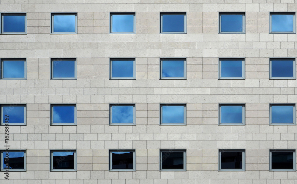Gray stone modern facade of a building with windows reflecting the sky