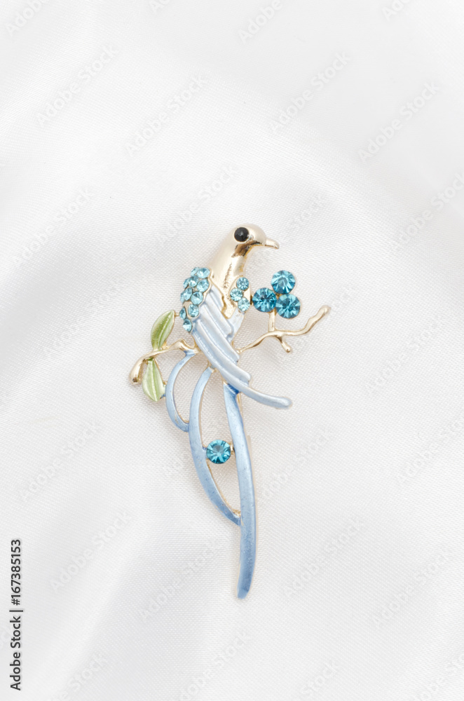 Golden brooch bird with blue stones on silk fabric Golden brooch bird with blue stones on silk fabric