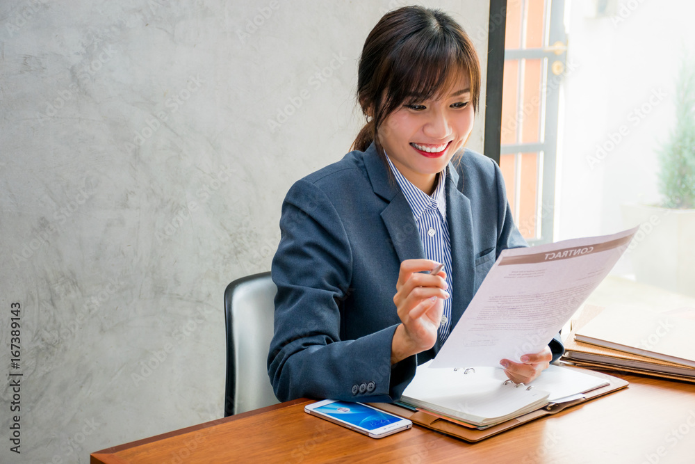 Young businesswoman who is wearing a blue jacket is reading and checking the information on the documents at the office Young businesswoman who is wearing a blue jacket is reading and checking the information on the documents at the office