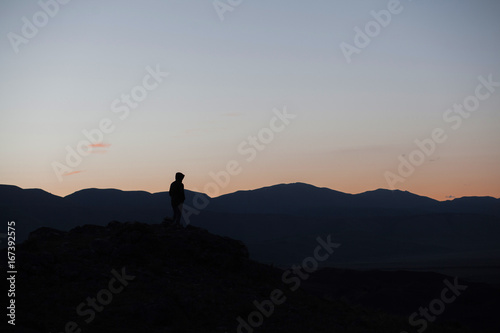 Man silhouette stay on sharp rock peak. Satisfy hiker enjoy view. Tall man on rocky cliff watching down to landscape.