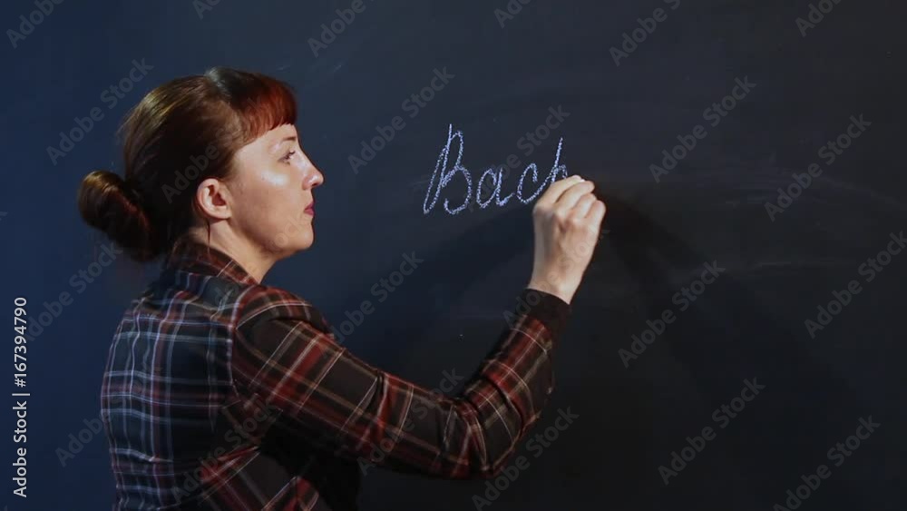 An experienced female teacher, with blue eyes in a tartan jacket, writes with a chalk on a blackboard An experienced female teacher, with blue eyes in a tartan jacket, writes with a chalk on a blackboard