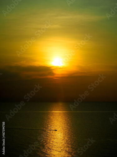 Silhouette photo of fisherman rowing a fishing boat in the middle of the sea. The light of the sunset in the evening reflects the beautiful golden sea.