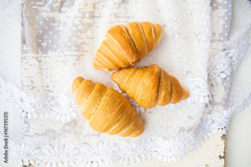 Beautiful and delicious croissants on the background of old laces and white table.