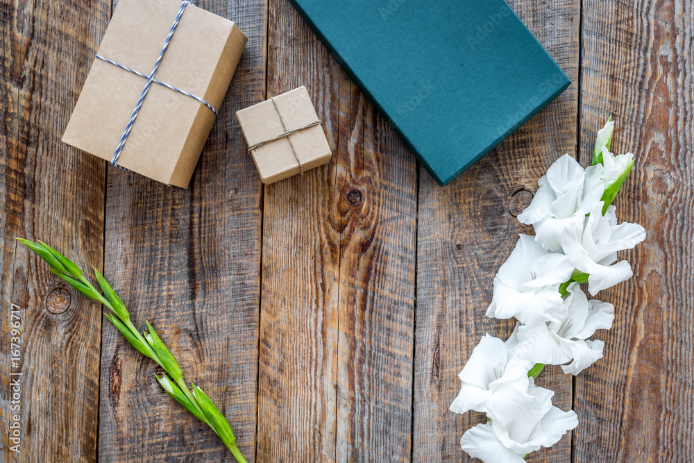 Gift box wrapped in craft paper near flower gladiolus on wooden background top view copyspace