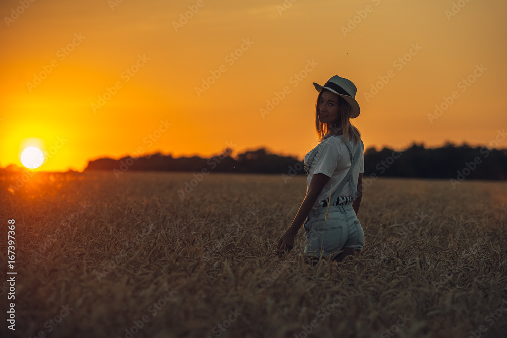 Young girl with outspread hands standing standing in the wheat field at sunset