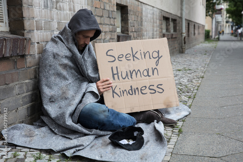 Beggar Showing Seeking Human Kindness Sign On Cardboard photo
