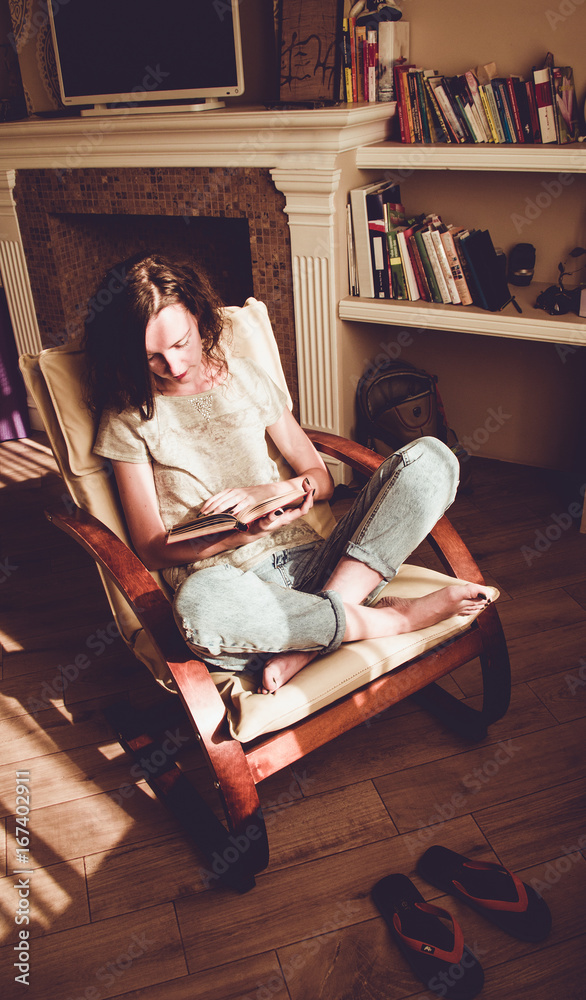 Enjoying time at home. Woman relaxing in comfortable modern chair reading paper book. Natural light. Cozy home. Enjoy moment. Bright sunny day. Knowledge, learning concept. Bookworm student. Vertical Enjoying time at home. Woman relaxing in comfortable modern chair reading paper book. Natural light. Cozy home. Enjoy moment. Bright sunny day. Knowledge, learning concept. Bookworm student. Vertical
