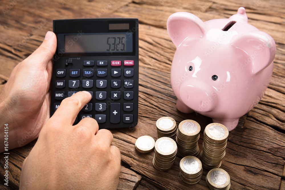 Businessman Using Calculator By Coins And Piggybank On Table Businessman Using Calculator By Coins And Piggybank On Table