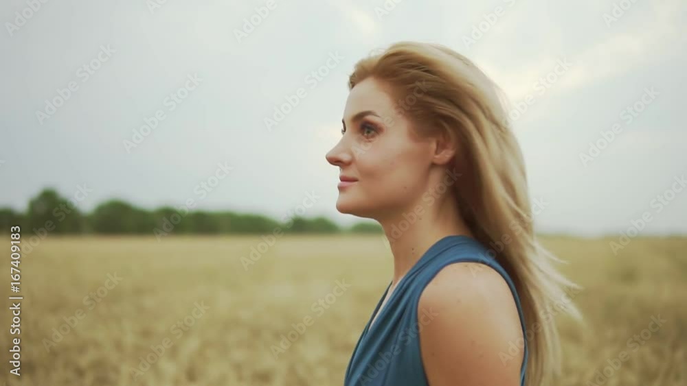 Closeup view of attractive young blond woman in a blue dress walking through golden wheat field. Freedom concept. Slowmotion shot Closeup view of attractive young blond woman in a blue dress walking through golden wheat field. Freedom concept. Slowmotion shot