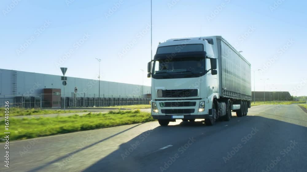Front-View Camera Follows Semi Truck with Cargo Trailer Driving on a Highway. He's Speeding Through Industrial Warehouse Area while Sun Shines and no other Vehicles are on the Road. Front-View Camera Follows Semi Truck with Cargo Trailer Driving on a Highway. He's Speeding Through Industrial Warehouse Area while Sun Shines and no other Vehicles are on the Road.