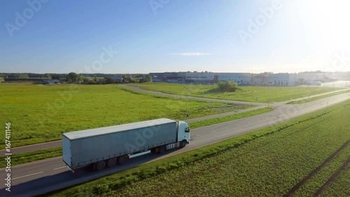 Aerial View of White Semi Truck with Cargo Trailer Moving on the Highway. In the Background Warehouses and Rural Area, Sun Shines. Shot on RED EPIC-W 8K Helium Cinema Camera. photo