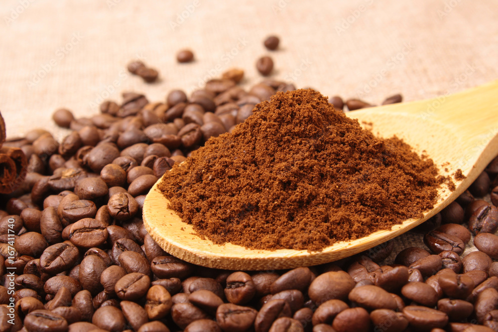 Ground coffee in a wooden spoon close-up on a background of coffee beans Ground coffee in a wooden spoon close-up on a background of coffee beans
