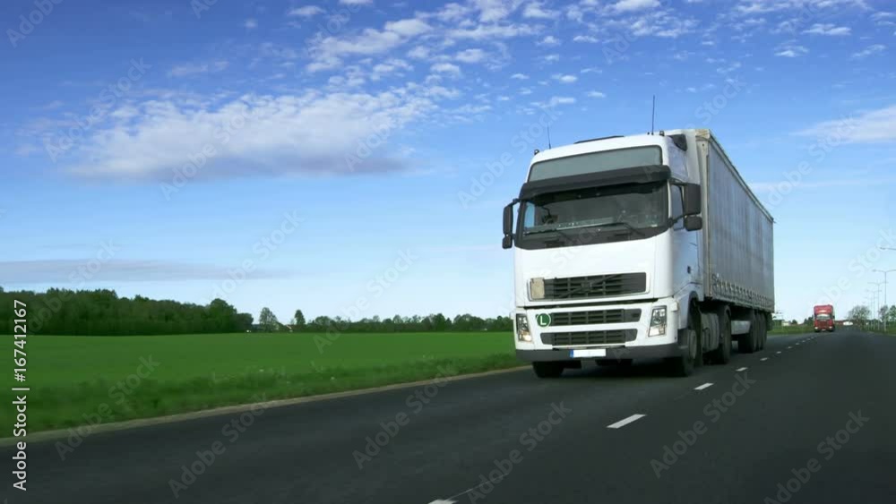 Speeding White Semi Truck with Cargo Trailer Drives on the Highway with Fields by the Sides of the Road. Shot on RED EPIC-W 8K Helium Cinema Camera. Speeding White Semi Truck with Cargo Trailer Drives on the Highway with Fields by the Sides of the Road. Shot on RED EPIC-W 8K Helium Cinema Camera.