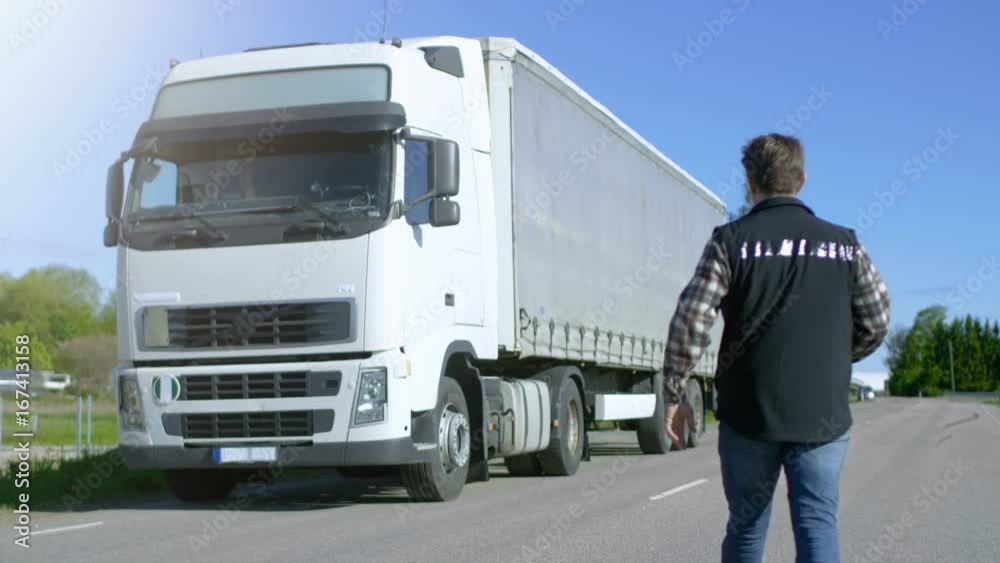 Truck Driver Crosses the Road and Gets into His Parked White Semi Truck with Cargo Trailer Attached. Sun Shines and Highway is Empty. Shot on RED EPIC-W 8K Helium Cinema Camera. Truck Driver Crosses the Road and Gets into His Parked White Semi Truck with Cargo Trailer Attached. Sun Shines and Highway is Empty. Shot on RED EPIC-W 8K Helium Cinema Camera.