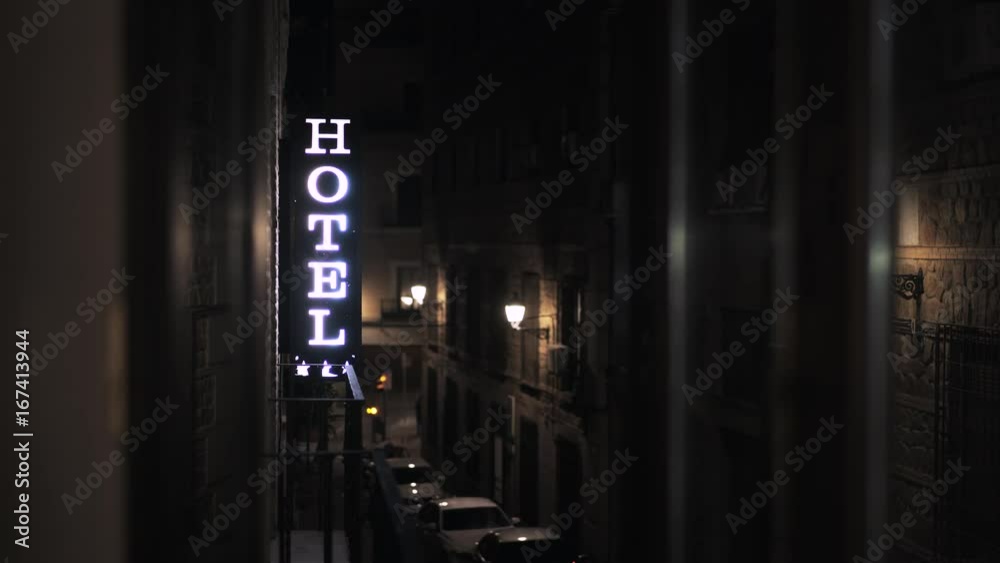 Close up of a shining Hotel sign in a street in Spain. Traffic lights in the background. Locked down real time close up shot Close up of a shining Hotel sign in a street in Spain. Traffic lights in the background. Locked down real time close up shot