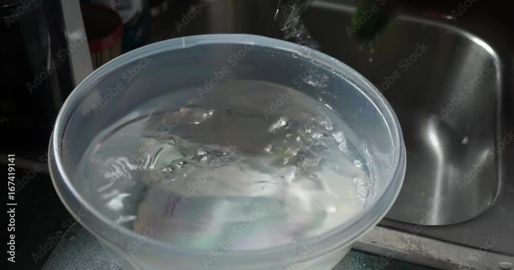 A person places three cucumbers into a bowl of water on a kitchen sink. Cleaning food, healthy lifestyle situation. A person places three cucumbers into a bowl of water on a kitchen sink. Cleaning food, healthy lifestyle situation.