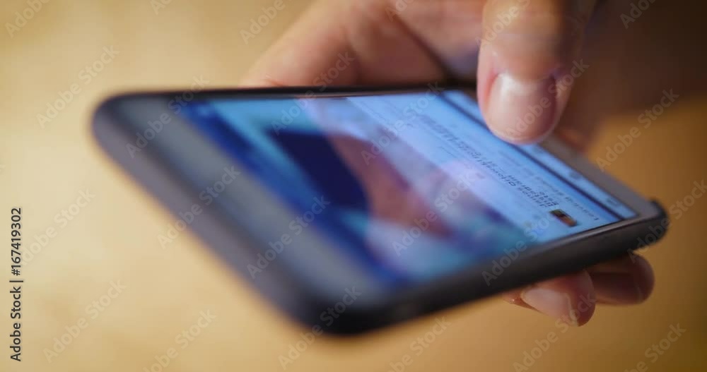 An extreme closeup with shallow DOF shot of someone scrolling through social media posts on a smartphone's touchscreen.  	
