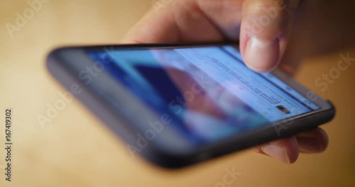 An extreme closeup with shallow DOF shot of someone scrolling through social media posts on a smartphone's touchscreen.  	