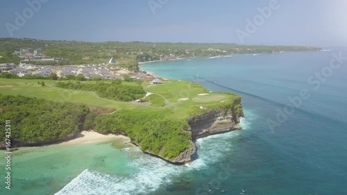 Aerial, lens flare flying above luxury bungalow tourist resort and new kuta golf course at the rim of the rocky and cliffy coastline overlooking vast blue ocean photo