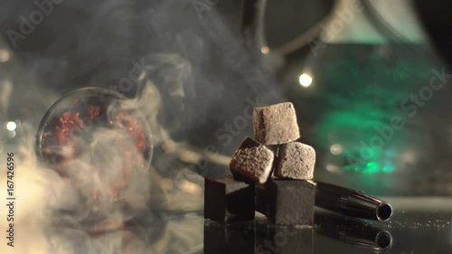 Close-up composition of the hookah embers laying near the hookah equipment on the table. The cloud of smoke is wrapping everything. photo