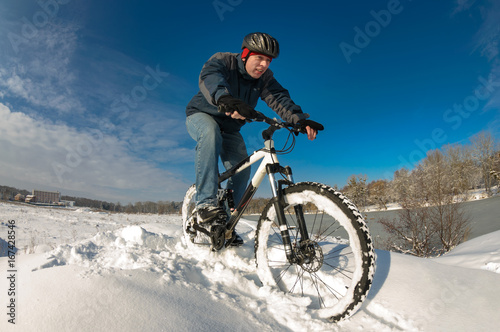 Man enjoys his ride on a bicycle in a deep snow, next to the river