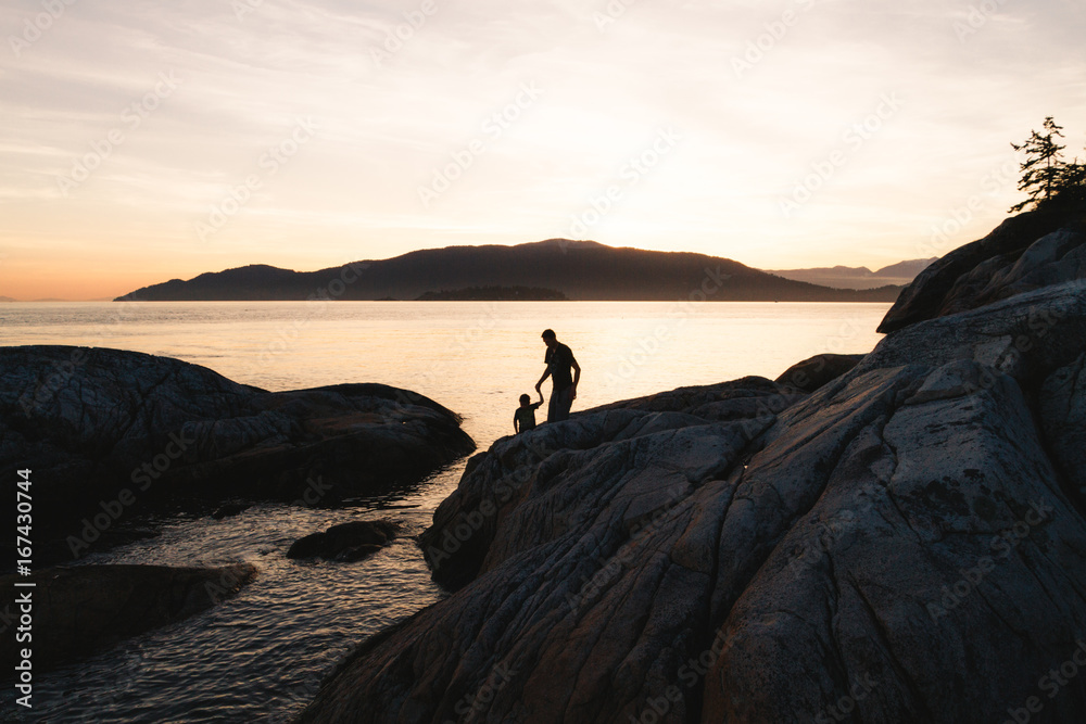 Father helping son on rocks while sunset