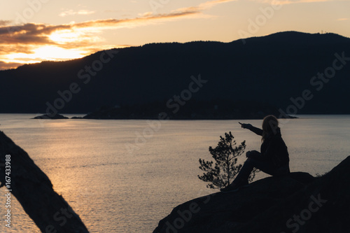 Silhouette of woman on coast with ocean and mountains while sunset