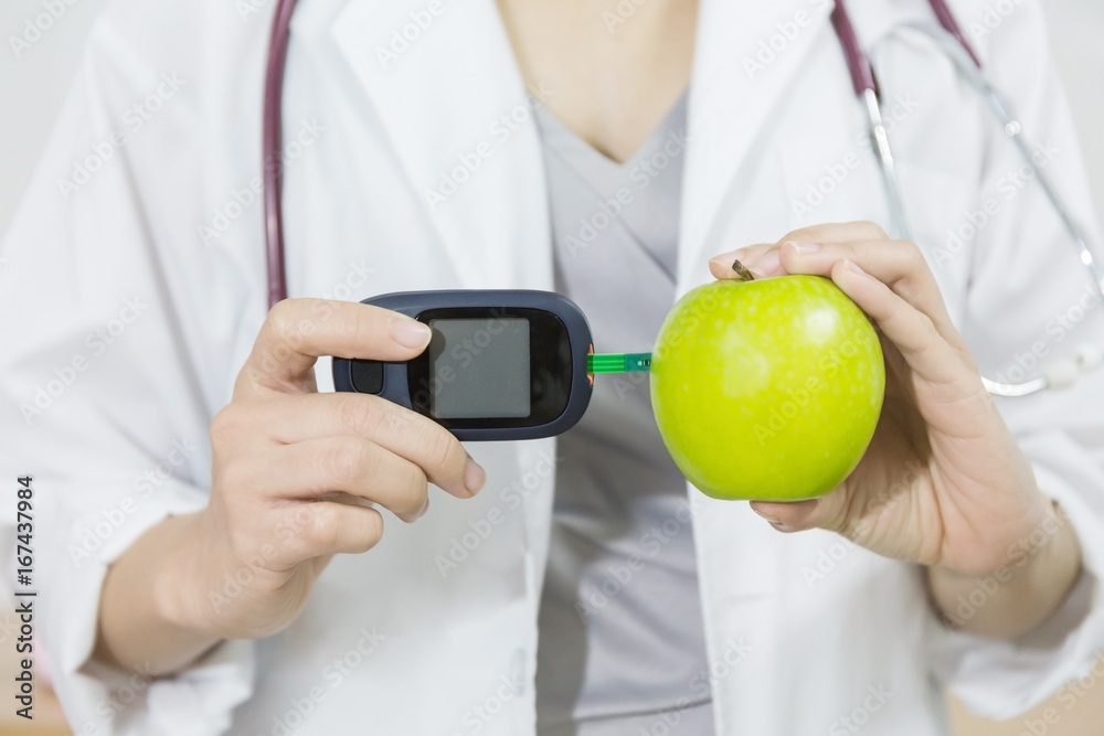Doctor using a glucometer to measure a glucose level in apple, Apple is a low glucose index level. Healthy food concept, Diabetes diet concept. Doctor using a glucometer to measure a glucose level in apple, Apple is a low glucose index level. Healthy food concept, Diabetes diet concept.