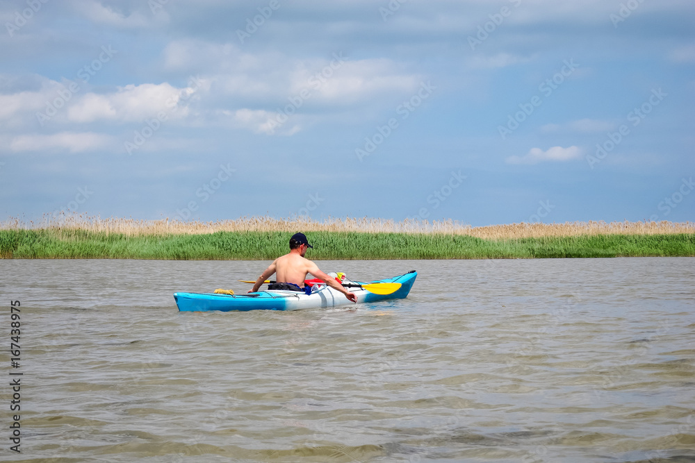 Man in blue kayak in life jacket kayaking in wild Danube river near confluence of the Danube in the Black sea
