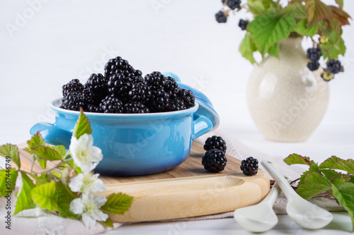 Ripe blackberries with leaves in a blue ceramic bowl on white table