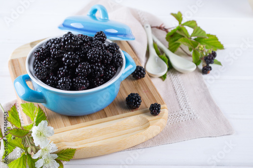 Composition of branch of Blackberry with leaf and  blackberries in a blue ceramic bowl on white table. 