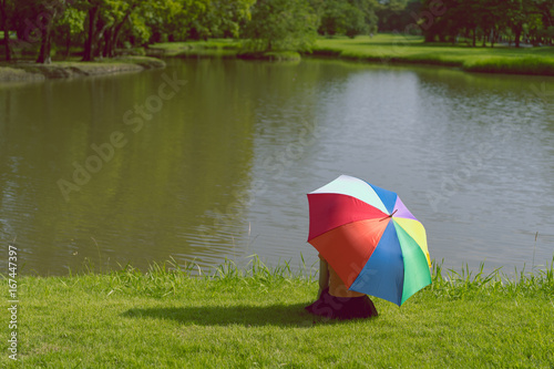 Fototapeta Naklejka Na Ścianę i Meble -  Young girl sitting alone with colorful umbrella at park