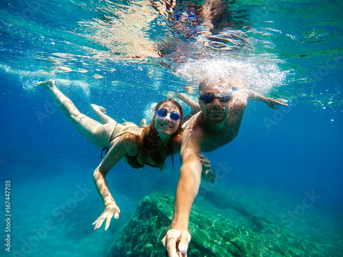 Joyful happy couple having fun underwater with selfie stick.