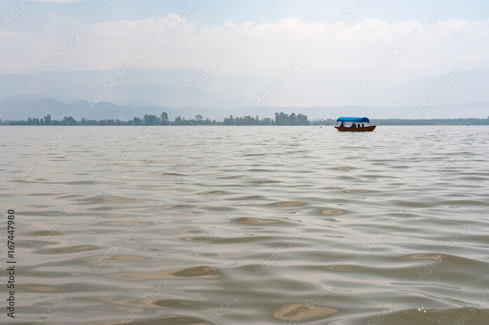 Small boat on a lake in the haze with mountains in the background, Xichang, China