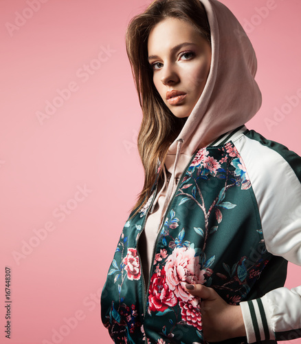Portrait of a stylish girl in a bomb jacket with floral print standing on a pink background