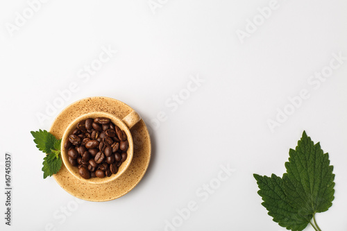 Coffee cup filled with coffee beans and green fresh leaves