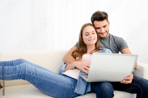 portrait of young and happy couple at home making project for future with laptop computer on internet