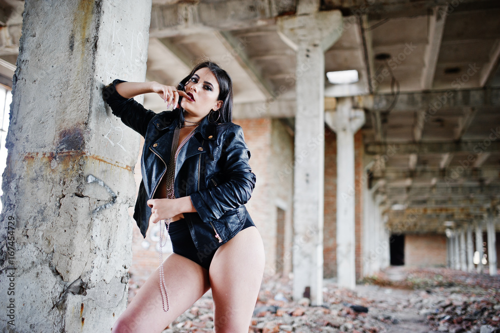 Brunette plus size sexy woman, wear at black leather jacket, lace panties at abadoned place. Woman's bare chest.
