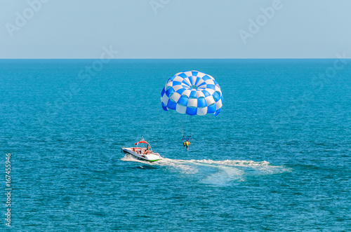 Obraz na plátně Blue parasail wing pulled by a boat in the sea water, Parasailing also known as