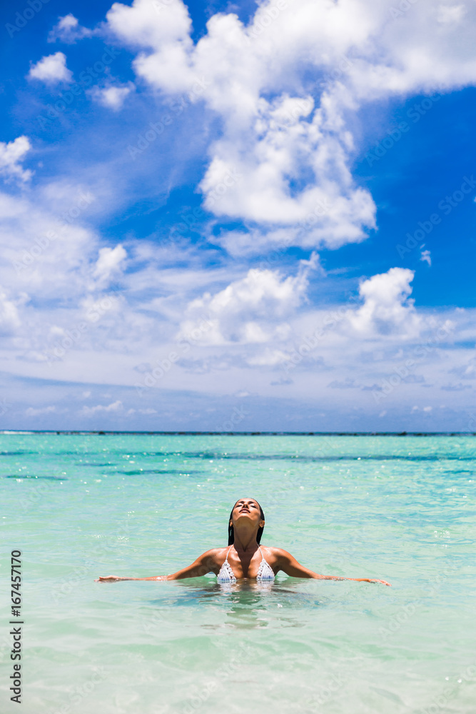Beautiful amazing sexy tanned girl lies in the water by the sea, enjoying the sun and warm water, relaxing on a tropical island, turquoise water, blue sky, summer style