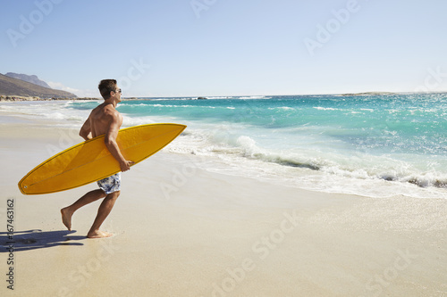 Surfer dude running to beach with yellow surfboard
