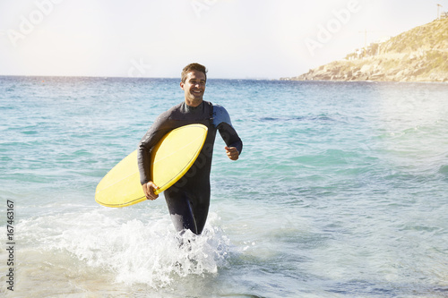 Surfer in wetsuit leaving sea with surfboard  smiling