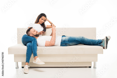 'portrait of young attractive couple using their smartphones on sofa, isolated on white