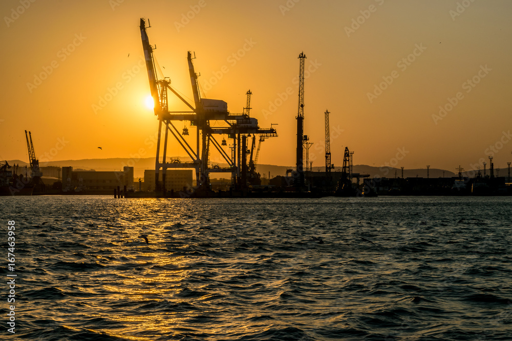 The silhouette of the port of Novorossiysk at sunset and the reflection of sunset in the waves of the uneasy Black sea