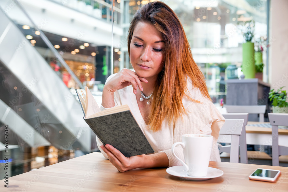 Relaxed girl reading book in cafe at shopping mall