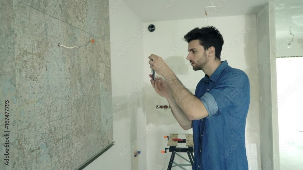 Young man taking photo of tiles with cellphone at his new home
